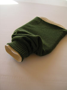 Slip the hot water bottle up through the wide end of the sleeve until the neck comes through the ribbed cuff and out of the body of the bottle.